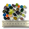 A selection of frosted glass beads in assorted sizes, shapes and colours with a ruler for size referral on a white background