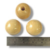 Three natural coloured wooden beads with a ruler for scale on a white background
